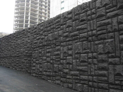Gray stone retaining wall with textured blocks next to unfinished high-rise building