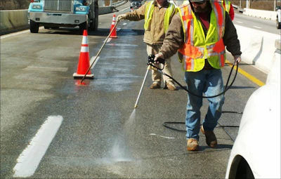 Road workers in high-visibility vests using spray equipment to mark highway lane