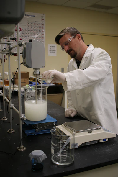 Lab technician in white coat mixing liquid in beaker on magnetic stirrer
