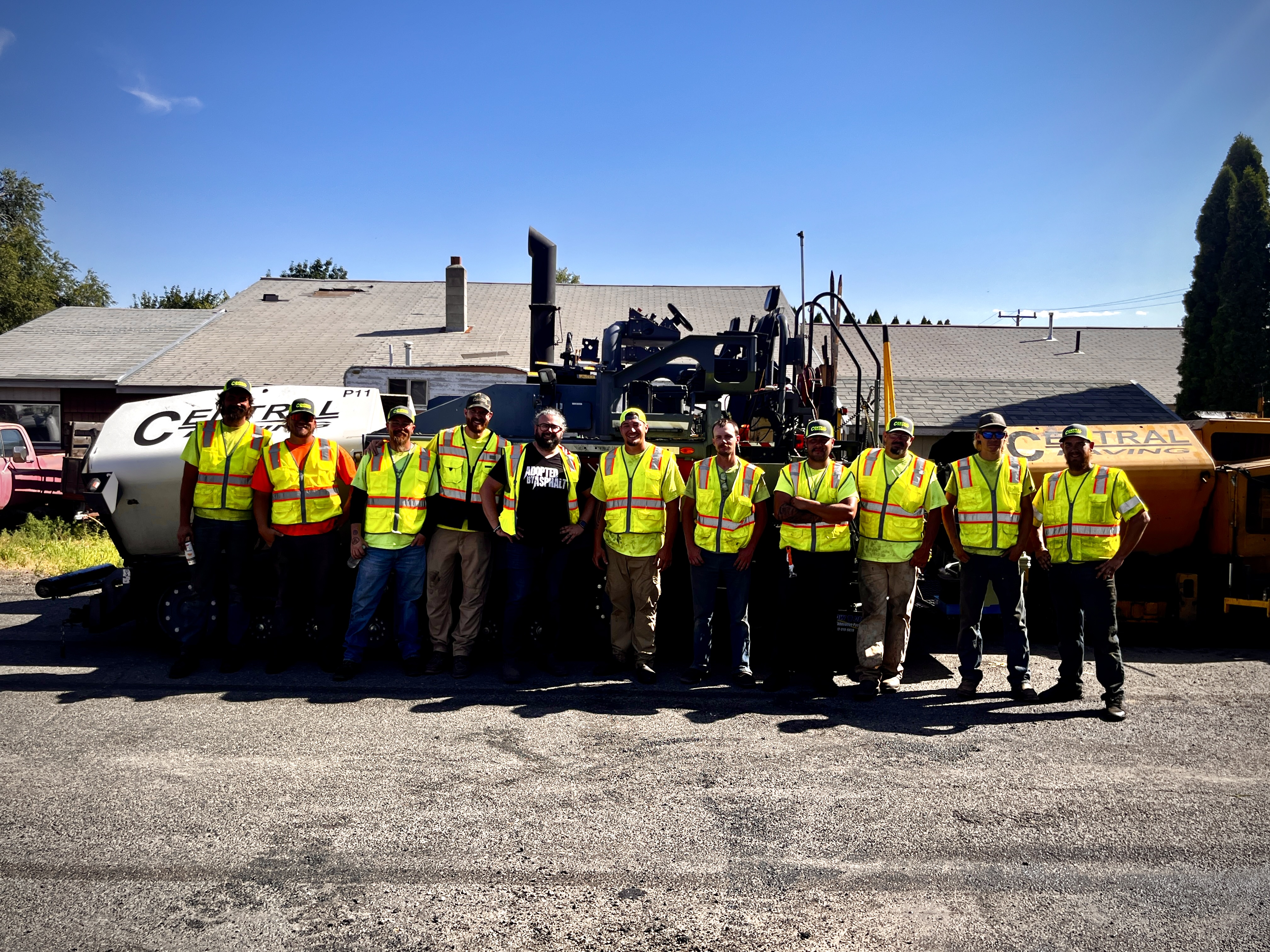 Construction crew in bright safety vests posing with road paving equipment