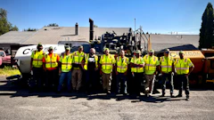 Construction crew in bright safety vests posing with road paving equipment