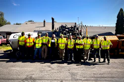 Construction crew in bright safety vests posing with road paving equipment