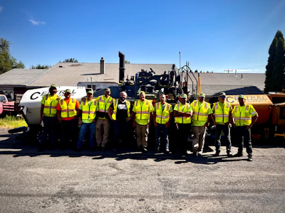 Construction crew in bright safety vests posing with road paving equipment