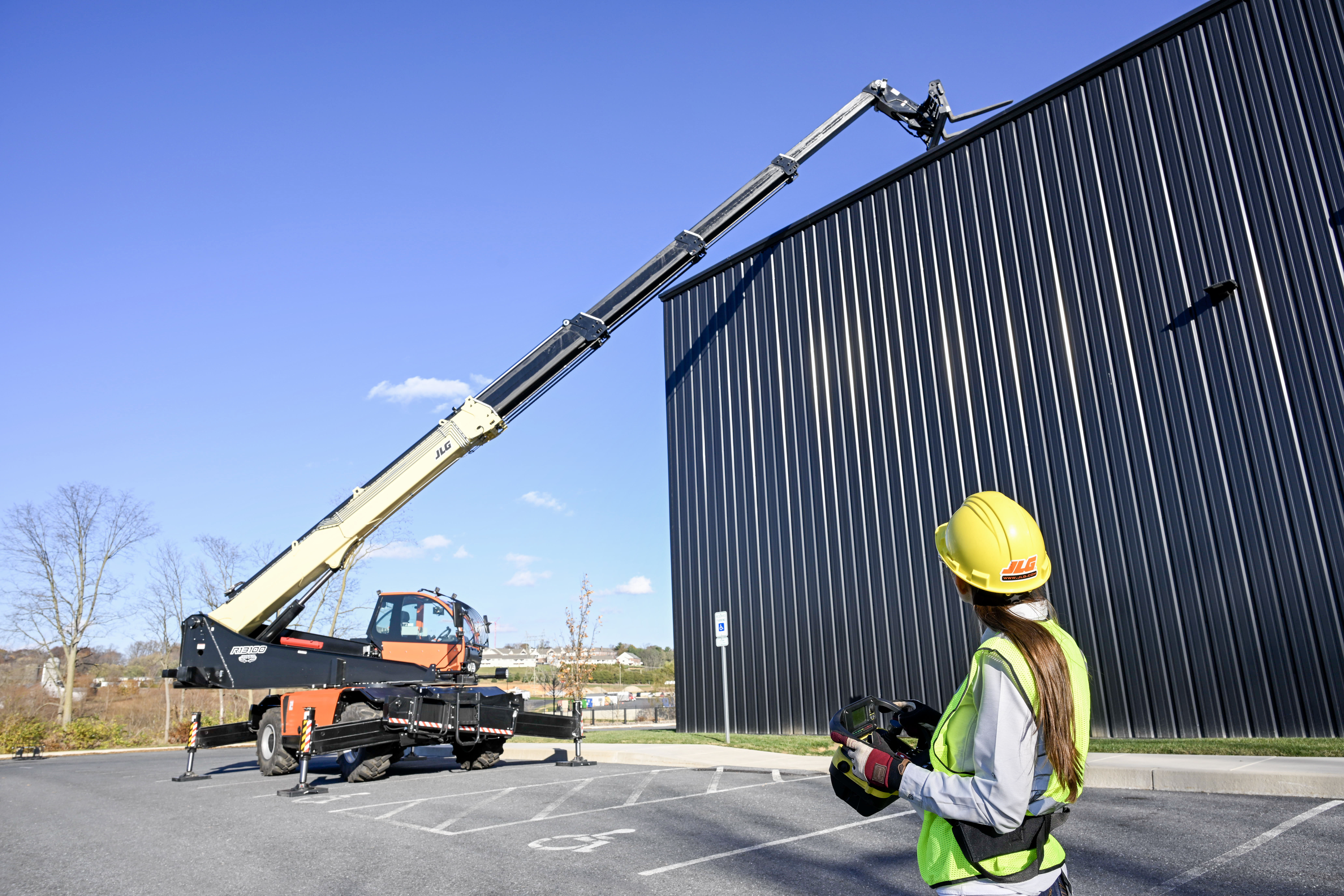 Construction worker operating mobile crane near metal warehouse building
