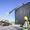 Construction worker operating mobile crane near metal warehouse building