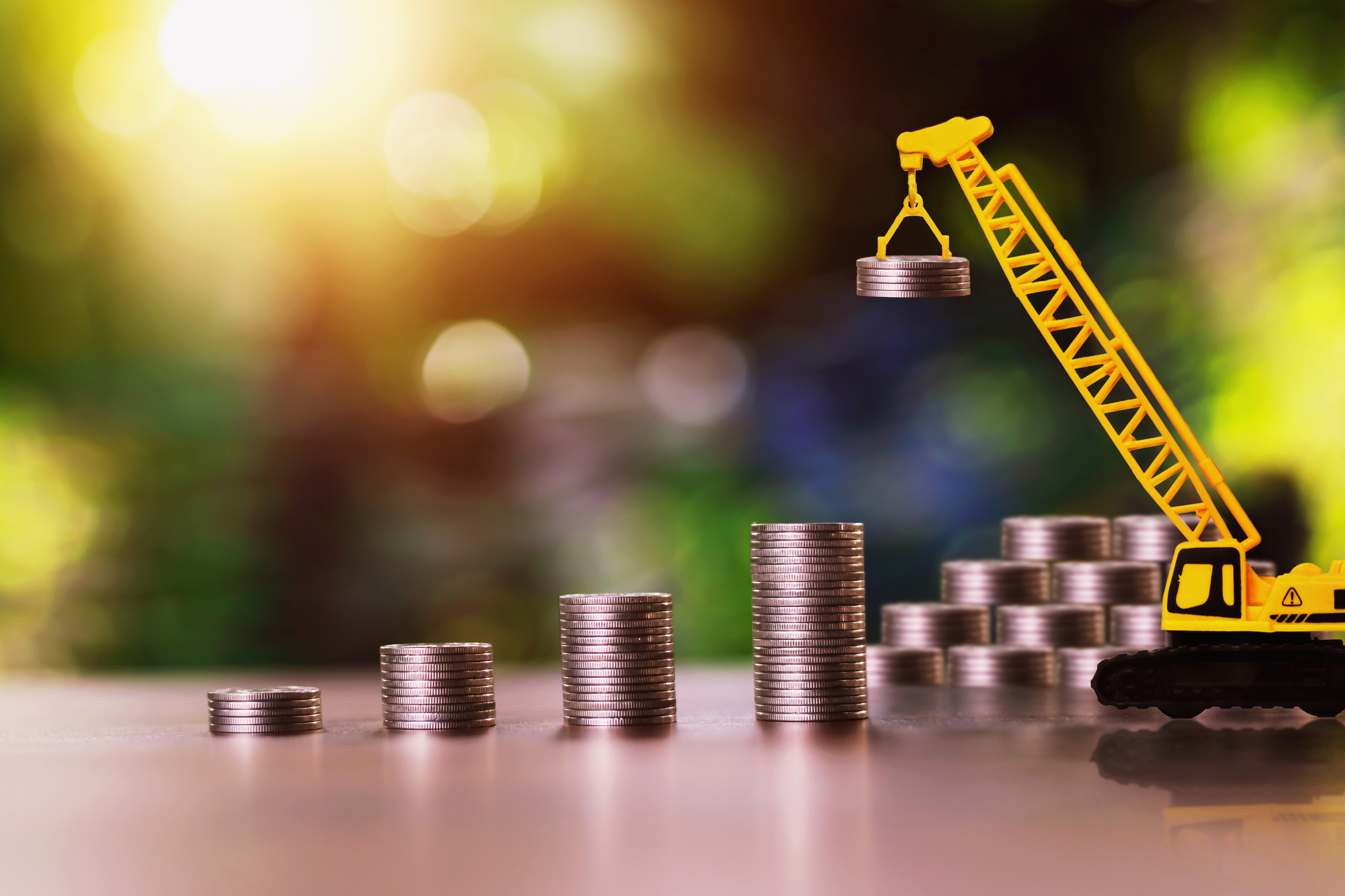 Yellow construction crane lifting coin stack, symbolizing financial growth and investment