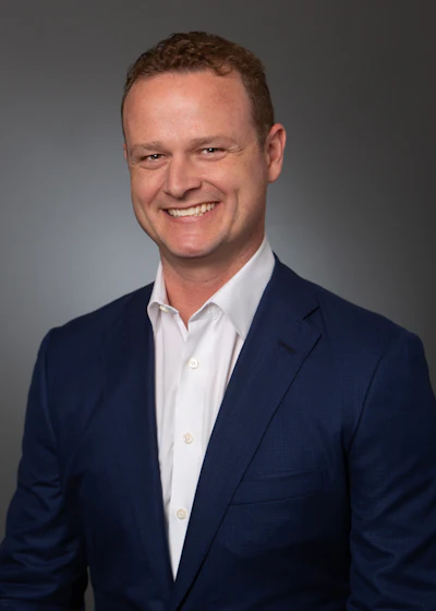 Smiling professional in navy suit against gray background