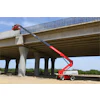 Red telescoping boom lift extending under concrete highway bridge during construction