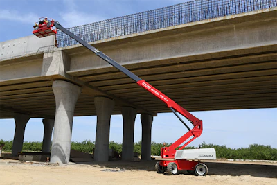 Red telescoping boom lift extending under concrete highway bridge during construction