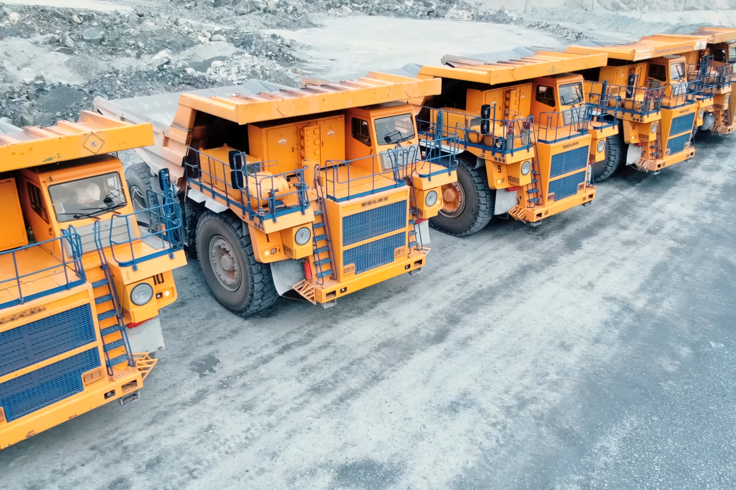 Large orange and blue mining haul trucks lined up on rocky terrain