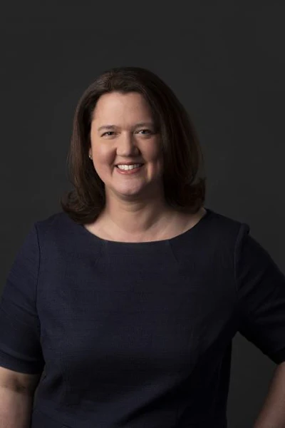 Smiling professional woman in navy blue top against dark background