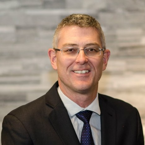 Professional man in glasses and dark suit smiling against textured background