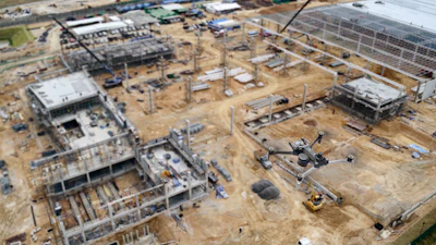 Aerial view of large construction site with multiple concrete buildings and drone