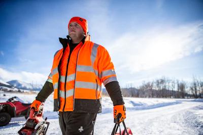 Worker in bright orange safety vest and gloves operating snow equipment
