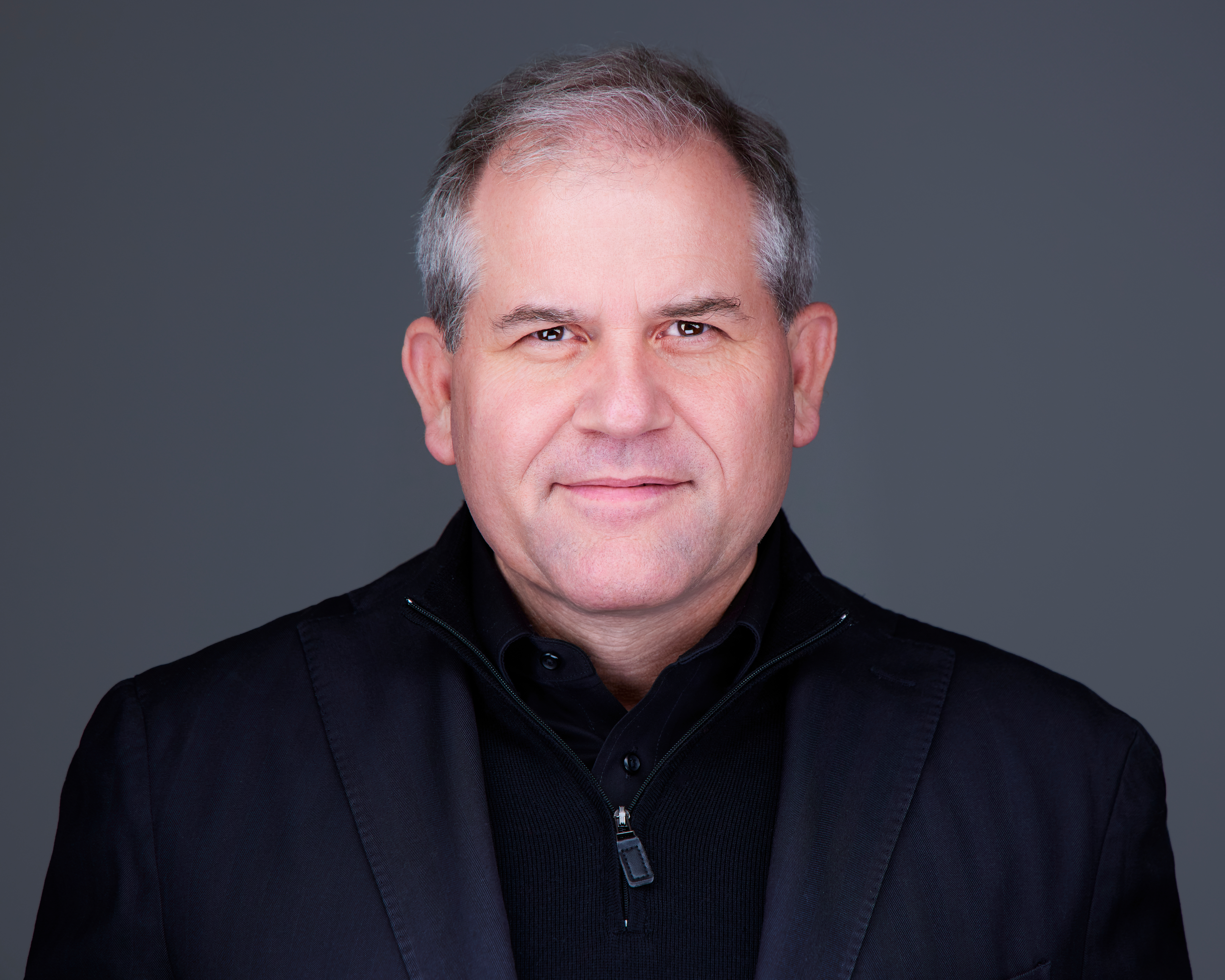 Professional headshot of a mature businessman in black attire against gray background Headshot