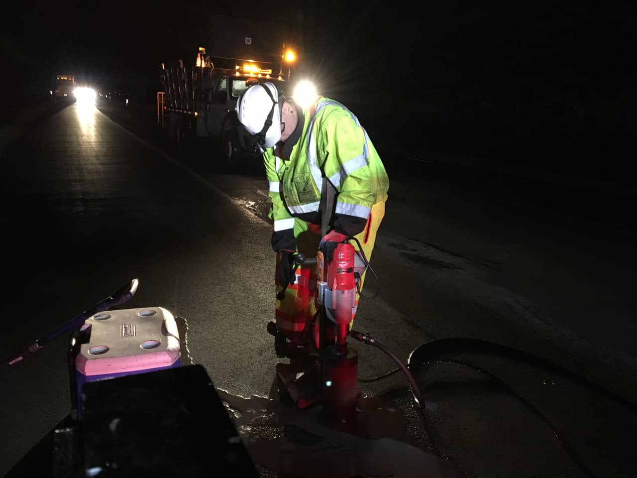 Road worker in neon safety vest operating road repair equipment at night