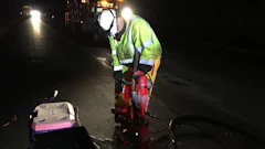 Road worker in neon safety vest operating road repair equipment at night