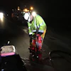 Road worker in neon safety vest operating road repair equipment at night