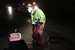 Road worker in neon safety vest operating road repair equipment at night