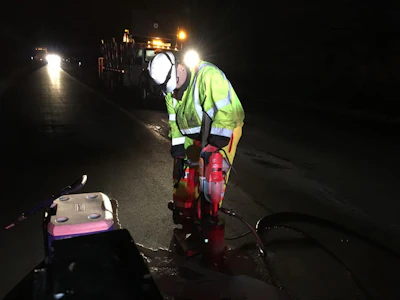 Road worker in neon safety vest operating road repair equipment at night
