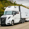 White Volvo autonomous semi-truck driving on highway with trees in background