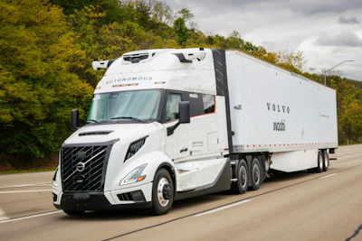 White Volvo autonomous semi-truck driving on highway with trees in background