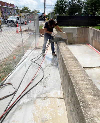 Construction worker using circular saw on concrete structure near chain-link fence