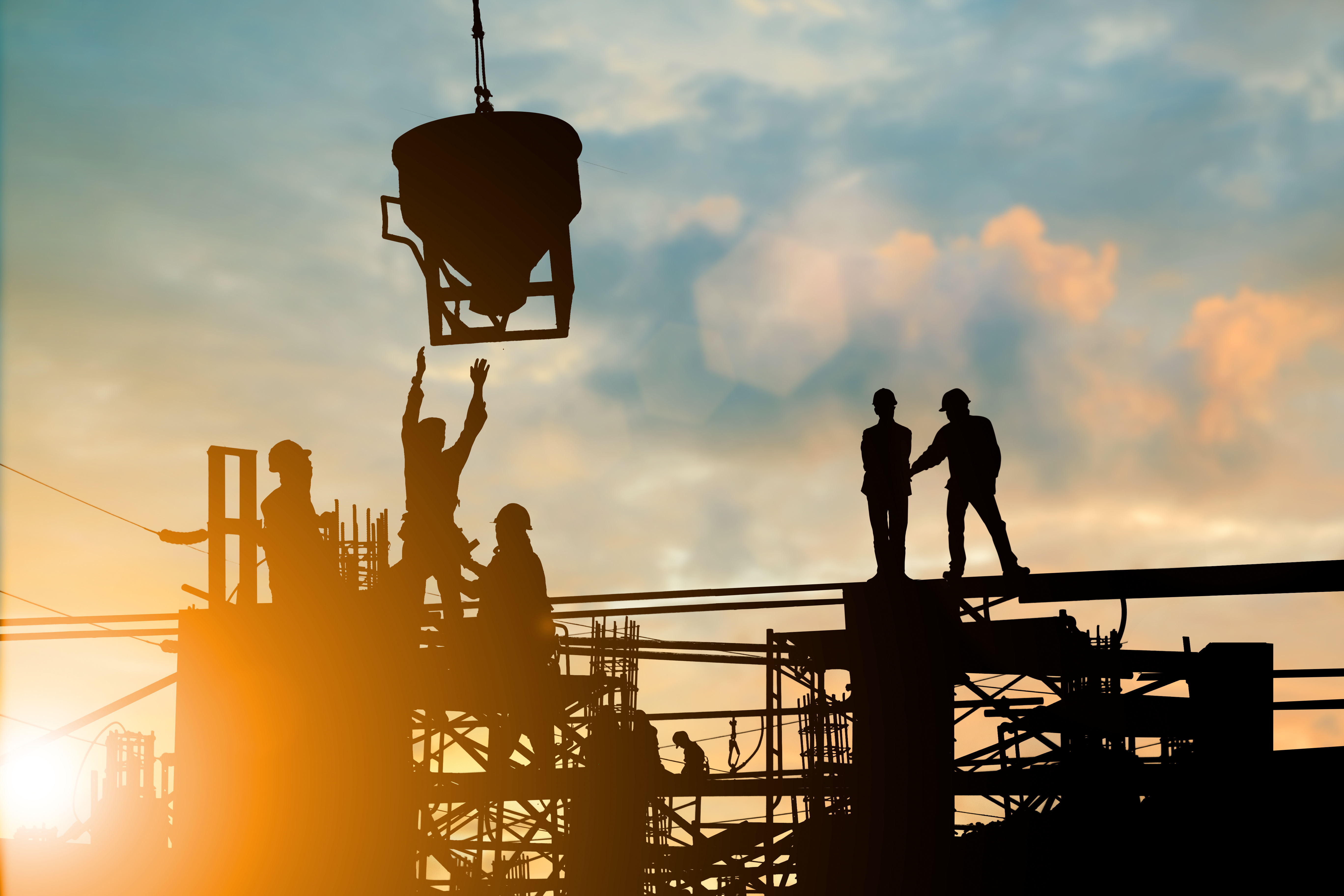 Construction workers on scaffolding at sunset, operating concrete pouring equipment