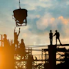Construction workers on scaffolding at sunset, operating concrete pouring equipment