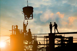 Construction workers on scaffolding at sunset, operating concrete pouring equipment