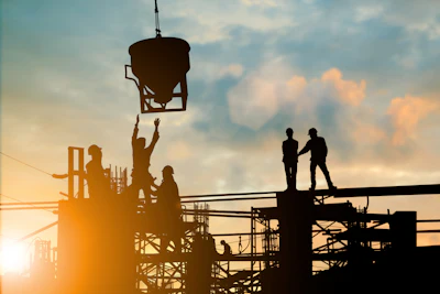 Construction workers on scaffolding at sunset, operating concrete pouring equipment