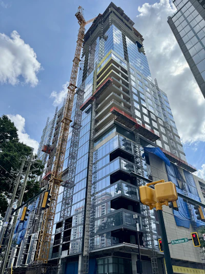 Modern glass skyscraper under construction with yellow crane, downtown urban setting