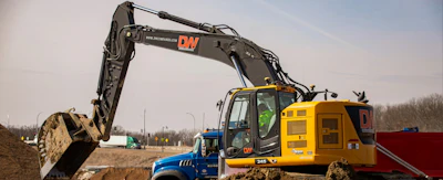 Yellow excavator and blue truck working on construction site with dirt mounds