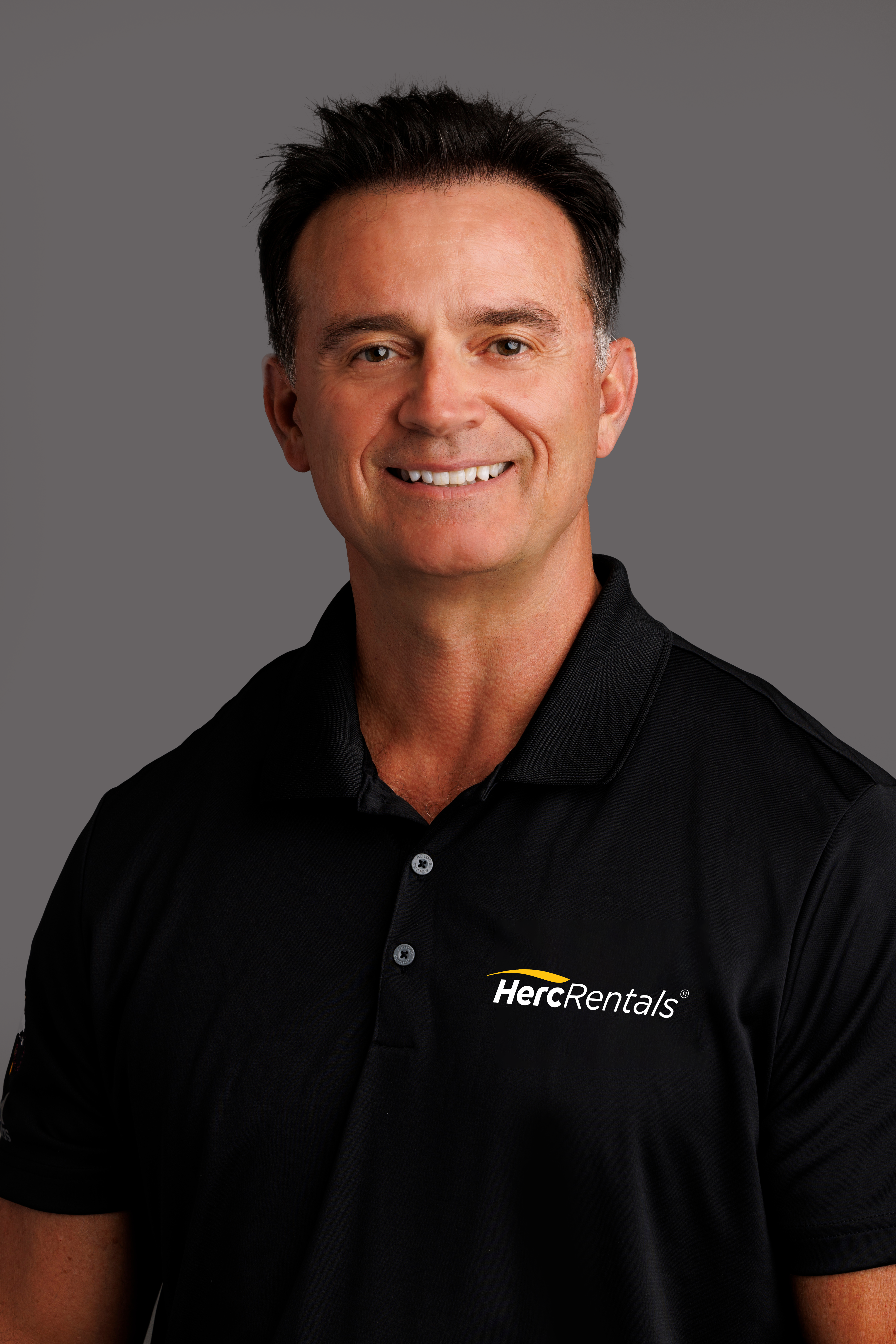 Smiling professional in black HercRentals polo shirt against neutral background