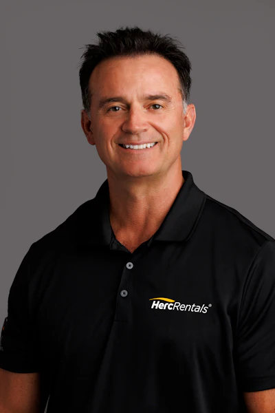 Smiling professional in black HercRentals polo shirt against neutral background