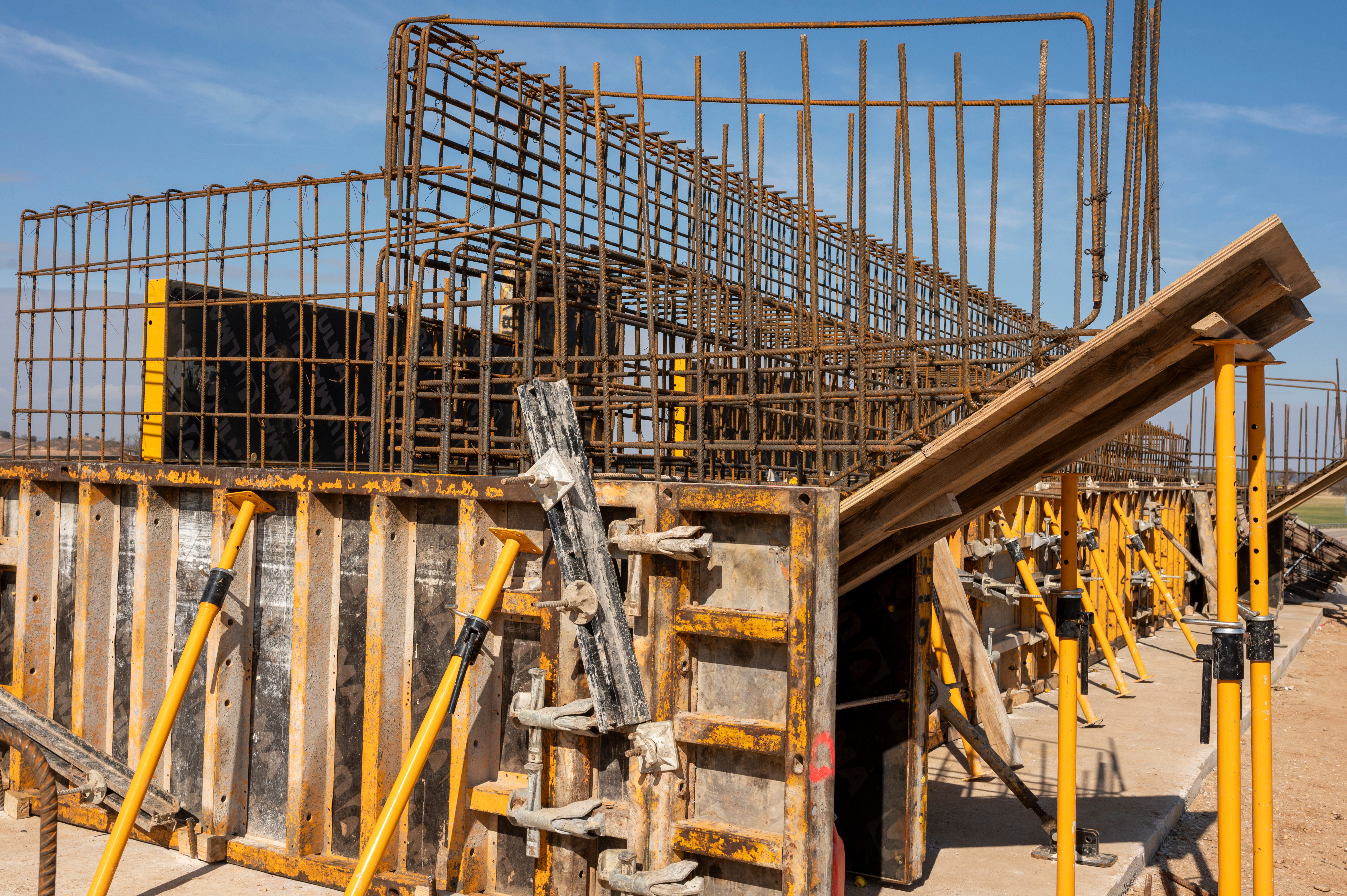 Construction site with steel rebar frames and yellow scaffolding supports