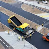 Road construction site with yellow paver, orange roller, and workers laying fresh asphalt