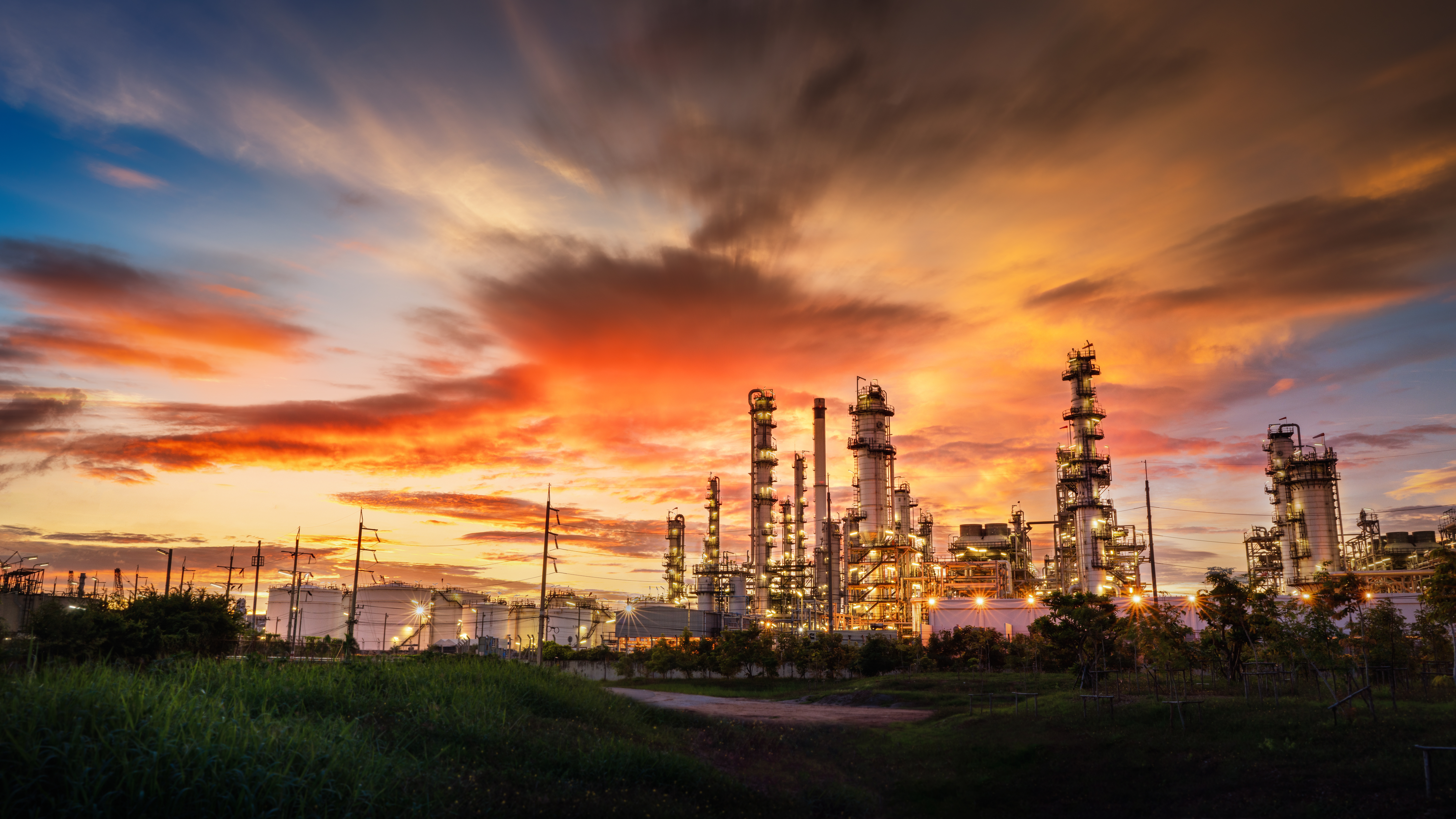 Oil refinery with towering industrial structures against a dramatic orange and blue sunset sky