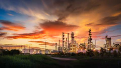Oil refinery with towering industrial structures against a dramatic orange and blue sunset sky