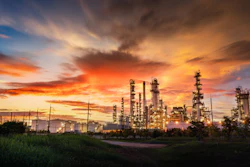 Oil refinery with towering industrial structures against a dramatic orange and blue sunset sky