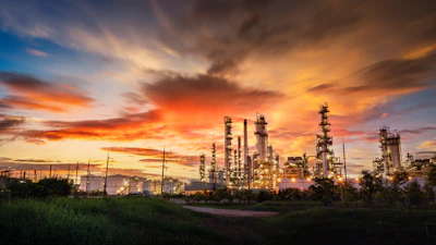 Oil refinery with towering industrial structures against a dramatic orange and blue sunset sky