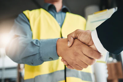 Construction professional in safety vest shaking hands with business colleague