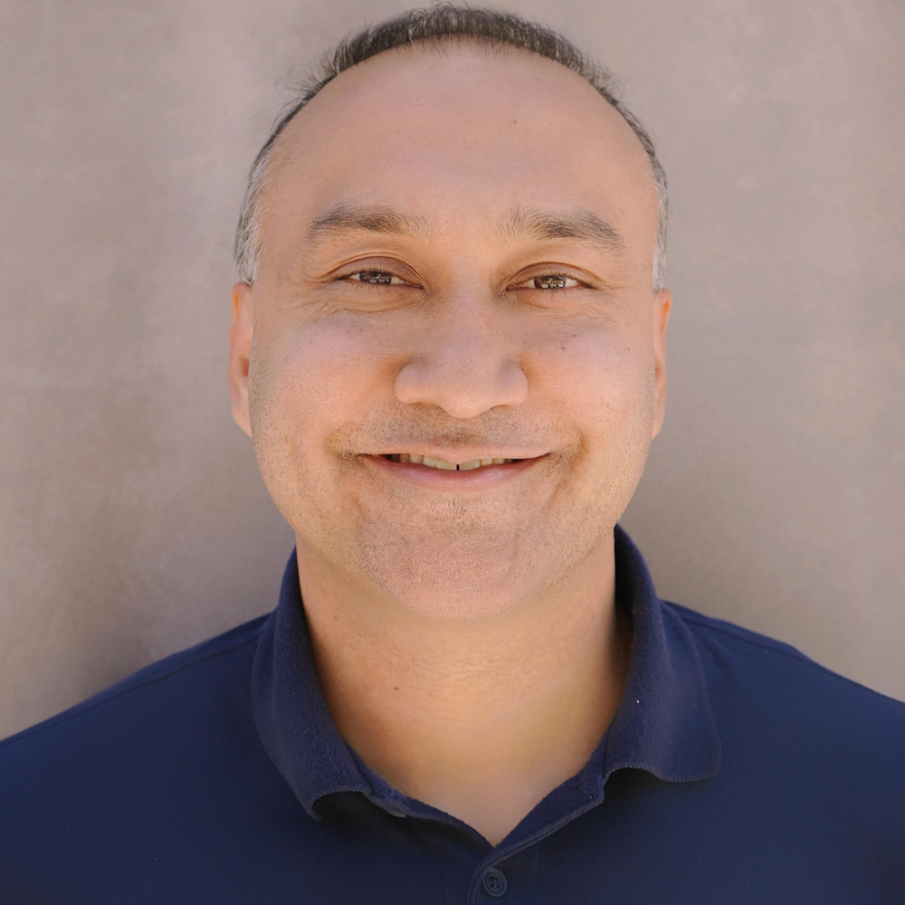 Middle-aged professional smiling warmly in navy blue polo shirt Headshot