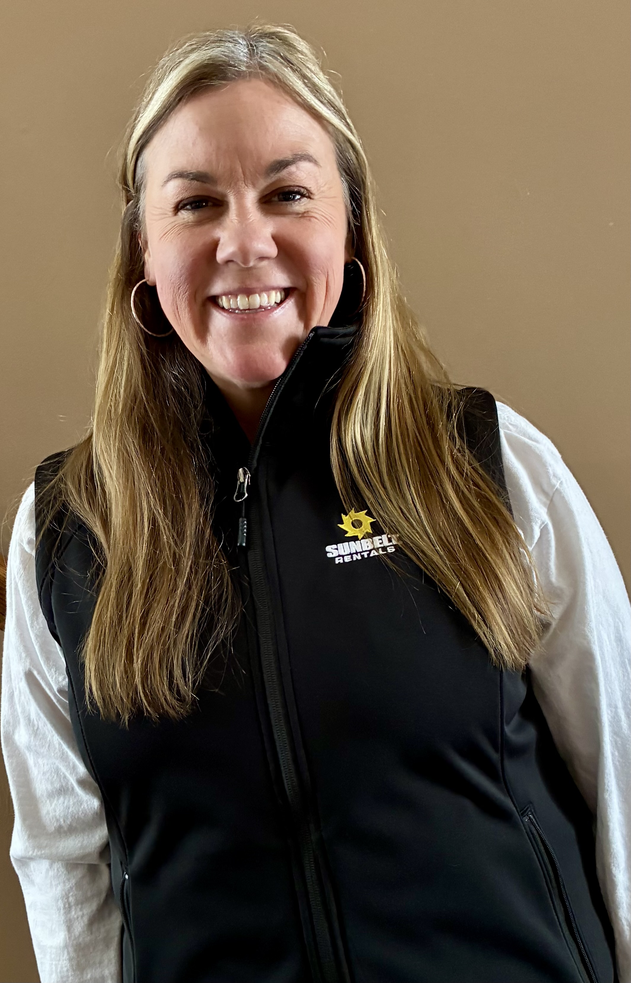 Smiling woman in white shirt and black Sunbelt Rentals vest against neutral background