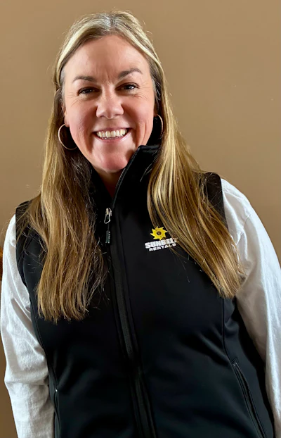 Smiling woman in white shirt and black Sunbelt Rentals vest against neutral background