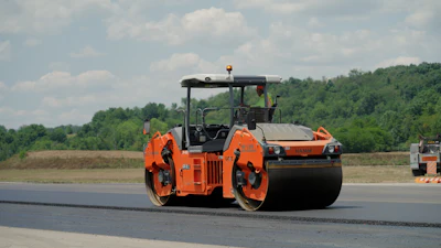 Orange road roller compacting fresh asphalt on highway construction site