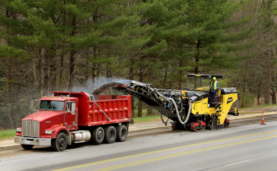 Road construction scene with red dump truck and yellow road milling machine on highway