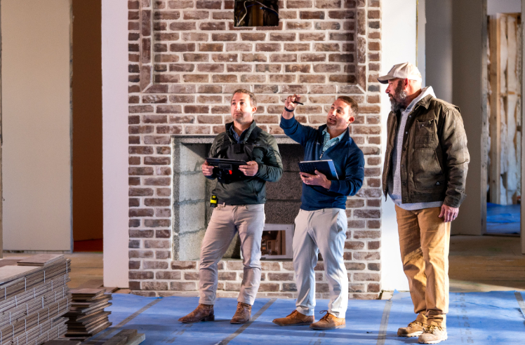 Three construction professionals reviewing plans near brick fireplace during site inspection