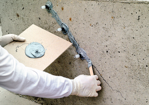 Construction worker's gloved hand drilling into concrete wall