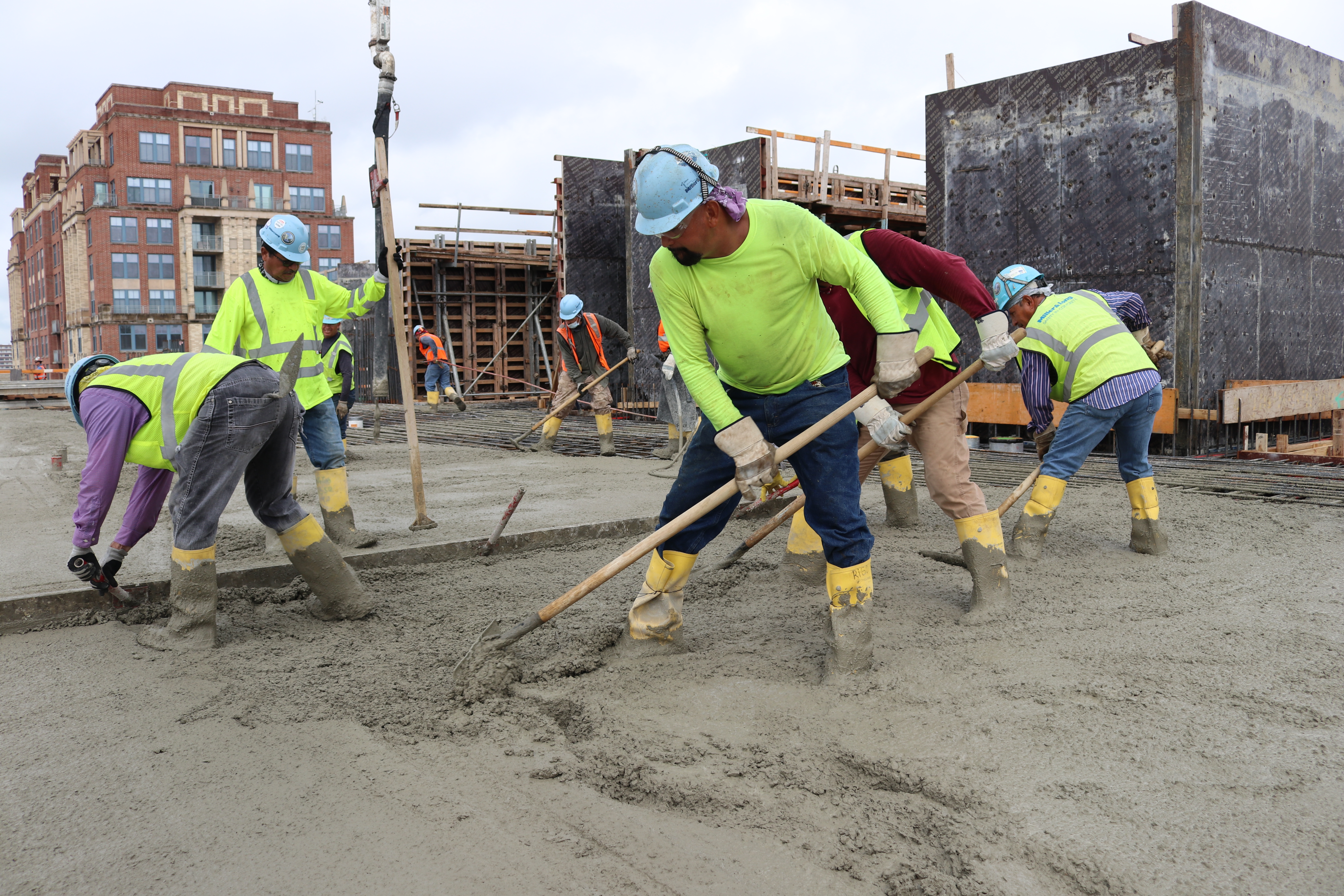 Construction workers in safety gear spreading concrete at urban building site